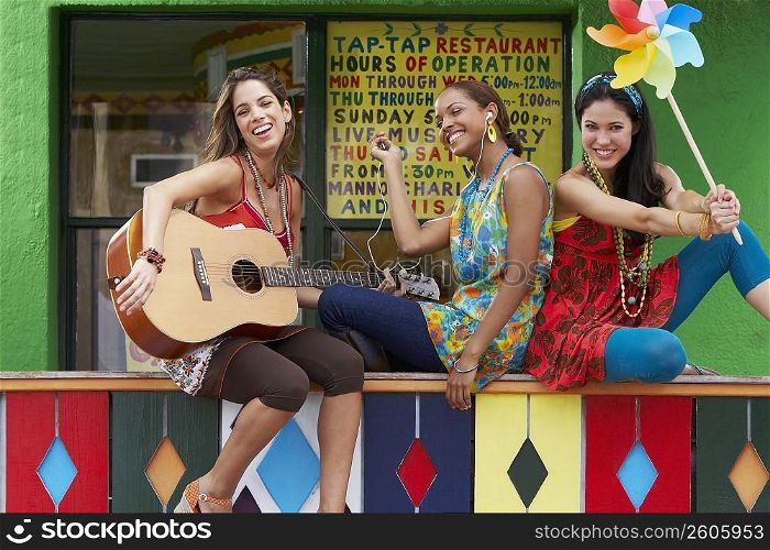 Young woman playing a guitar with her two friends holding a pinwheel and an ipod