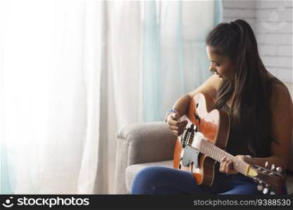Young woman playing guitar while sitting on sofa in living room