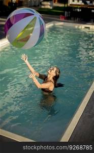 Young woman playing with a ball in the swimming pool at sunny day