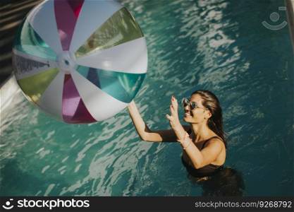 Young woman playing with a ball in the swimming pool at sunny day