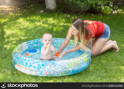 Young woman playing with her baby boy in inflatable pool at garden