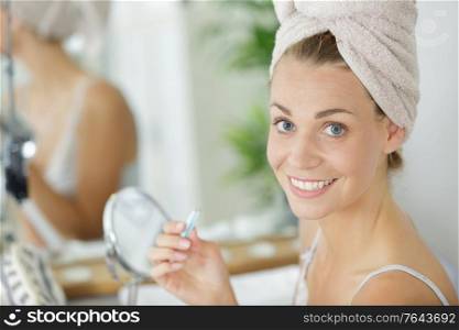 young woman plucking eyebrows with tweezers in front of mirror