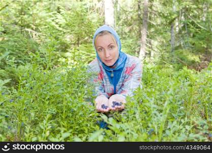 Young woman plucks bilberry in forest