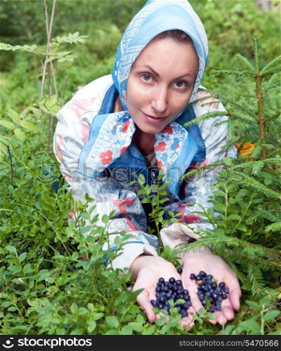 Young woman plucks bilberry in forest