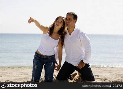 Young woman pointing forward to a mid adult man on the beach