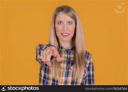 young woman pointing his finger toward camera against orange backdrop