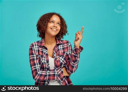 Young woman points up, blue background, positive emotion. Face expression, female person looking on camera in studio, emotional concept, feelings. Woman points up, blue background, positive emotion