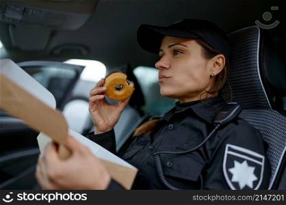 Young woman police officer eating sweet donut sitting in car during lunch break on work. Woman police officer eating donut in car