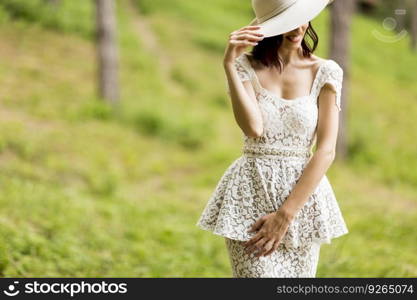 Young woman posing in a white dress with a hat in summer park