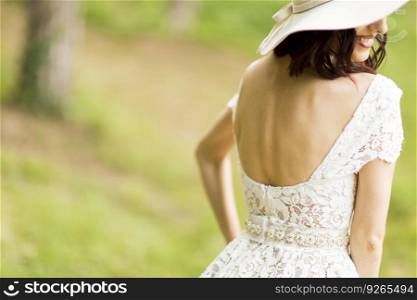 Young woman posing in a white dress with a hat in summer park