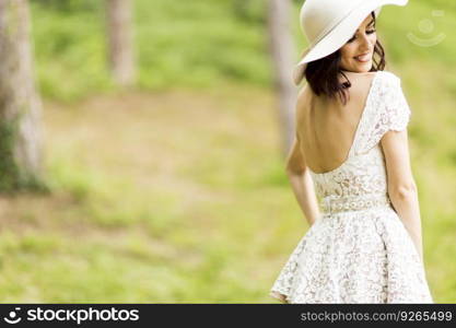 Young woman posing in a white dress with a hat in summer park