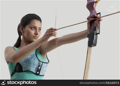 Young woman practicing archery against gray background