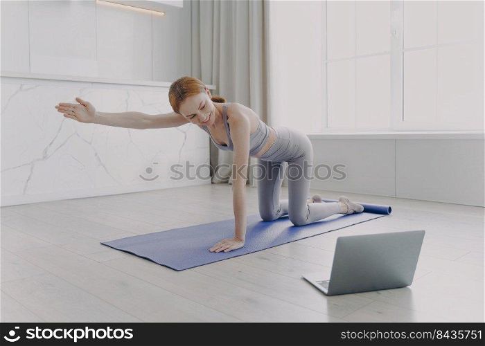 Young woman practicing yoga by video tutorial. European girl is looking at laptop screen. Posture exercise. Concept of internet learning and distance home classes on quarantine.. Young woman practicing yoga by video tutorial. Posture exercise. Home classes on quarantine.