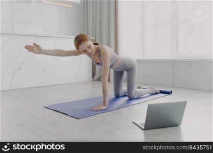 Young woman practicing yoga by video tutorial. European girl is looking at laptop screen. Posture exercise. Concept of internet learning and distance home classes on quarantine.. Young woman practicing yoga by video tutorial. Posture exercise. Home classes on quarantine.