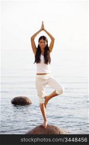 Young woman practicing yoga near the ocean