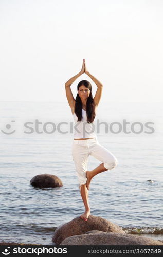 Young woman practicing yoga near the ocean