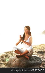 Young woman practicing yoga near the ocean