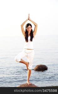 Young woman practicing yoga near the ocean