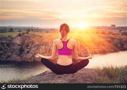 Young woman practicing yoga on the hill at sunset near the river.