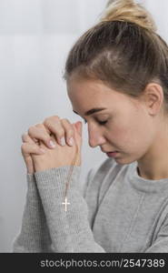 young woman praying home with cross necklace