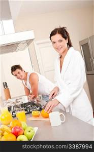 Young woman preparing breakfast in the kitchen, cutting orange