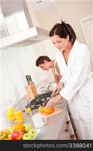Young woman preparing breakfast in the kitchen, cutting oranges