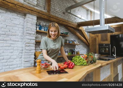 Young woman preparing food in the rustic kitchen while using digital tablet