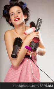 Young woman preparing for date having fun, cute girl with curlers styling hair with many accessories comb brush hairdreyer on gray