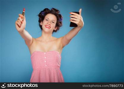 Young woman preparing to party, girl styling hair with curlers, applying makeup red lipstick retro style blue background