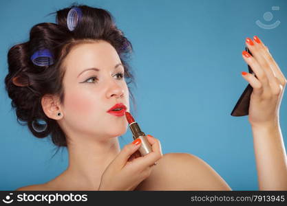 Young woman preparing to party, girl styling hair with curlers, applying makeup red lipstick retro style blue background