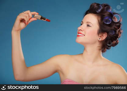 Young woman preparing to party, girl styling hair with curlers, applying makeup red lipstick retro style blue background