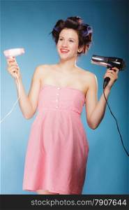 Young woman preparing to party having fun, funny girl styling hair with two hairdreyers retro style on blue