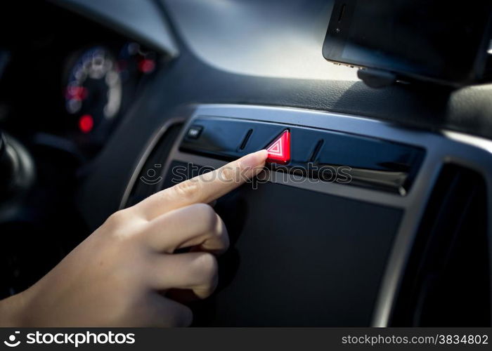 Young woman pressing emergency button on car dashboard