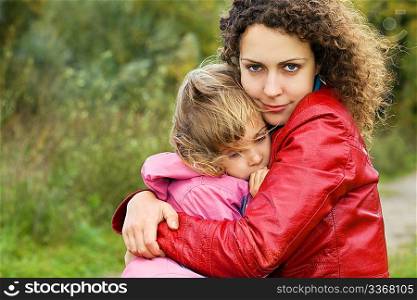young woman protects little girl from wind in garden