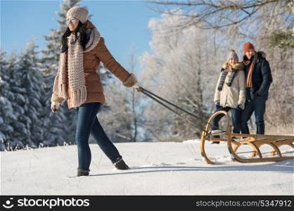 Young woman pulling winter sledge couple walking through snow countryside