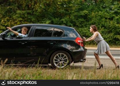 Young woman pushing broken car with man on road, breakdown. Crashed automobile or emergency accident with vehicle, trouble with engine on highway