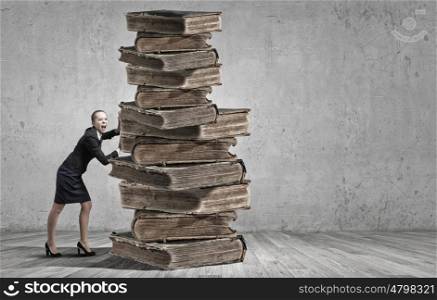 Young woman pushing huge pile of old books. Books and reading