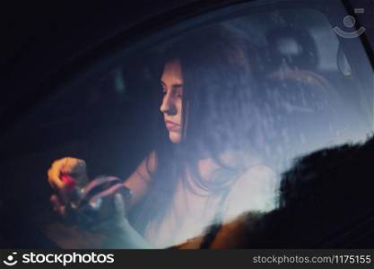 Young woman puts on makeup inside a car at sunset