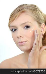young woman putting cream on her face