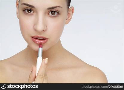 Young woman putting lipstick on her lips