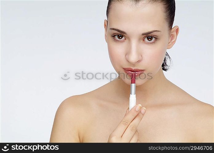 Young woman putting lipstick on her lips