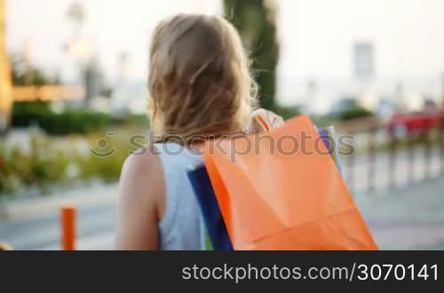 Young woman putting shopping bags on shoulder outdoor. She turning and smiling being satisfied with good shopping