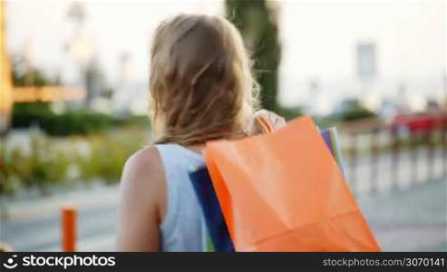 Young woman putting shopping bags on shoulder outdoor. She turning and smiling being satisfied with good shopping
