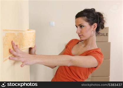 Young woman putting up wallpaper