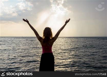 Young woman raising her arms by the sea