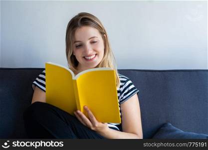 Young woman reading a book and lying on sofa at home.