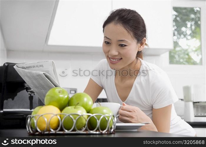 Young woman reading a newspaper and drinking tea in a domestic kitchen