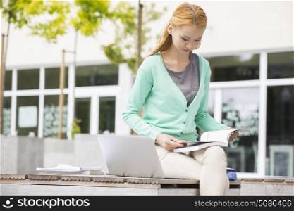 Young woman reading book at college campus
