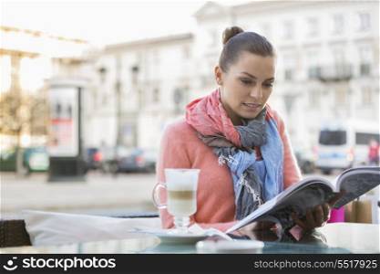 Young woman reading book at sidewalk cafe