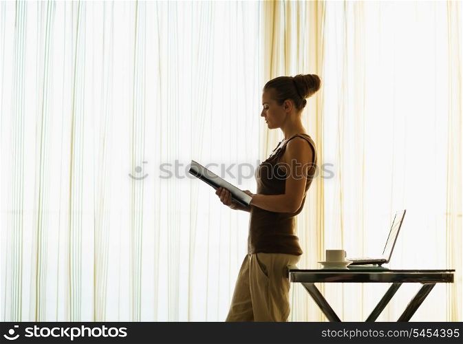 Young woman reading book leaning against table